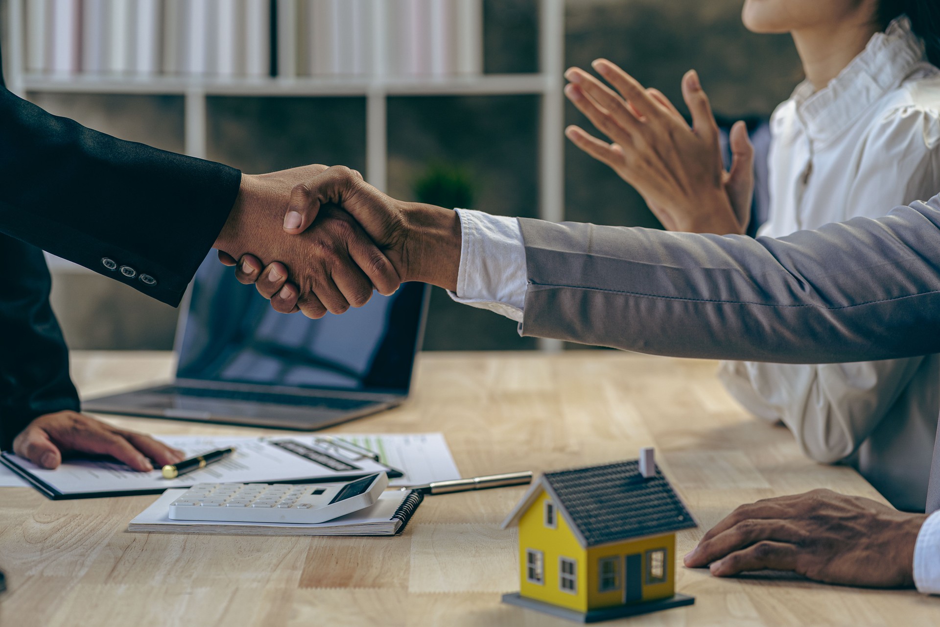 Successful negotiations and handshake of real estate purchase and sale. Home sales agent shaking hands with client after signing contract and completing home purchase at table in real estate office